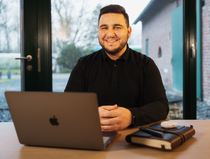 Davide Russo - Porträt Schreibtisch Porträt eines Geschäftsmannes am Schreibtisch mit aufgeklapptem Laptop, Notizbuch und Kopfhörern und Blick in die Kamera